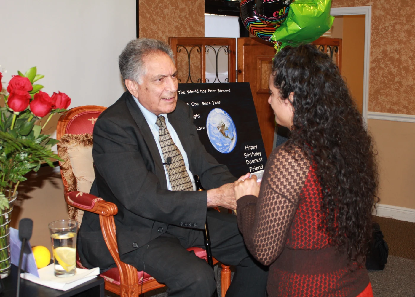 Ishwar Puri seated beside flowers, greeting a visitor
