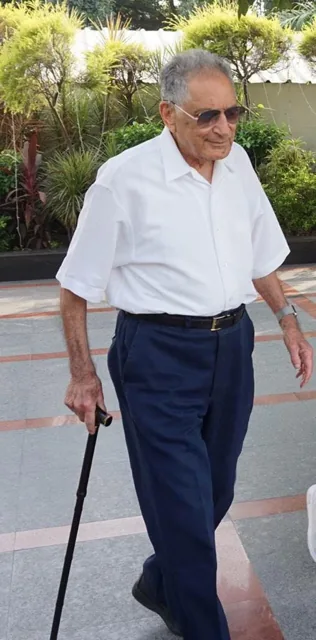 Ishwar Puri walking outdoors with a cane, wearing a white shirt