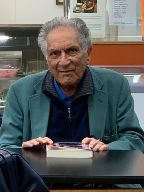 Ishwar Puri seated at a table, wearing a green jacket