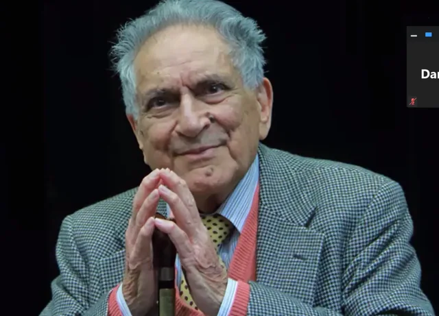Ishwar Puri greeting the audience with his palms together, wearing a gray jacket